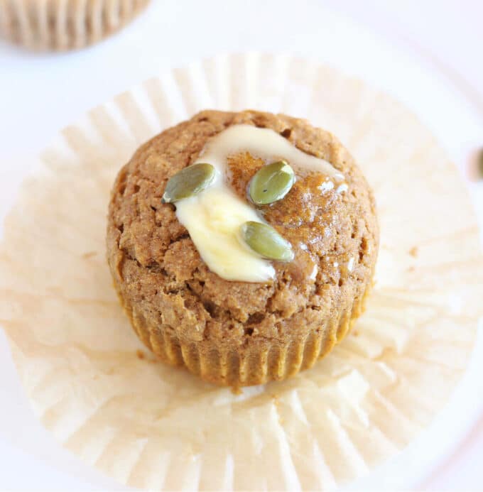 Pumpkin muffin on a wrapper with butter and pumpkin seeds on top.