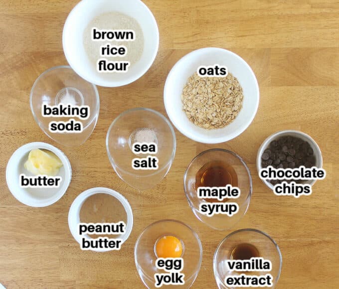 Ingredients, such as rice flour, oats, and maple syrup, laid out on a wood table.
