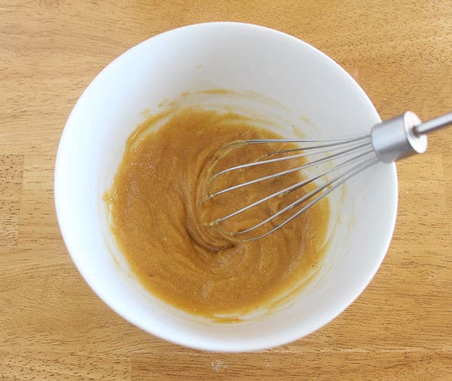 Whisking a brownish-orange batter in a white bowl.