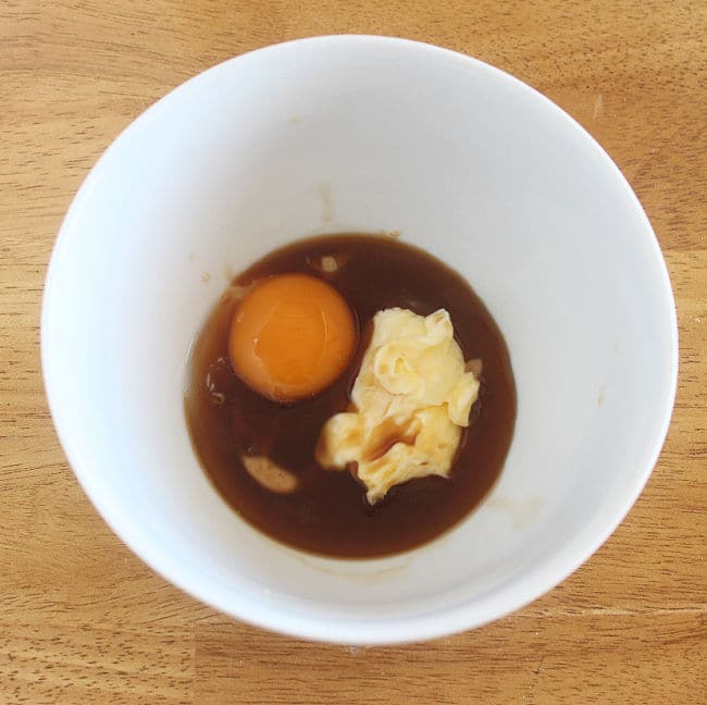 Egg yolk, chunk of butter, and brown liquid in a white bowl.