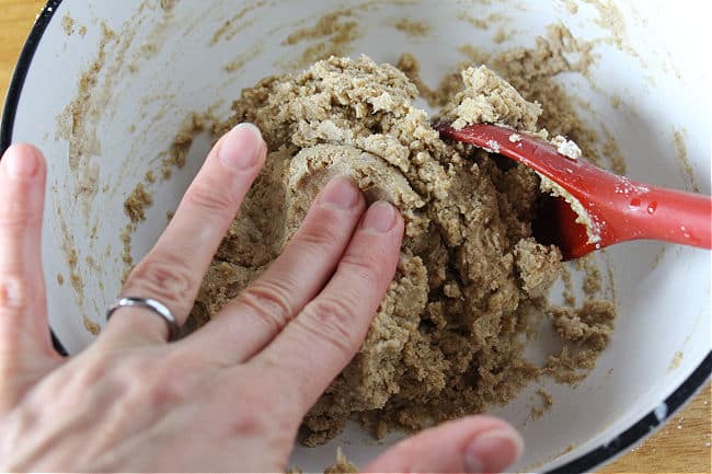 Fingers touching dough in a white bowl.