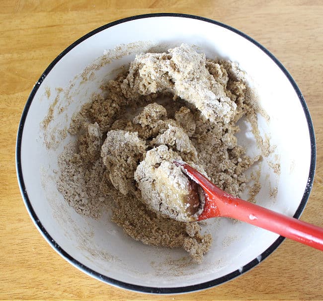 Dough in a bowl being stirred by a red spoon.