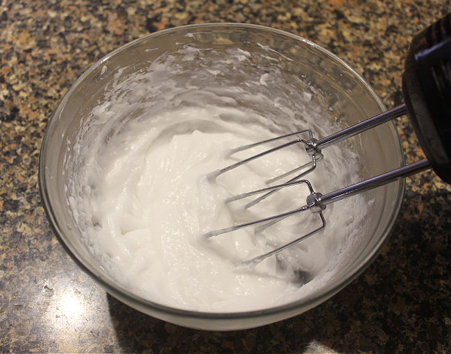 Hand mixer whipping coconut oil in a glass bowl.