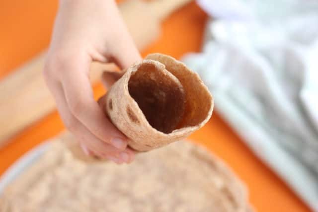 Hand holding a spelt flour tortilla rolled up.