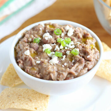 Bowl full of refried pinto beans topped with scallions and queso fresco.