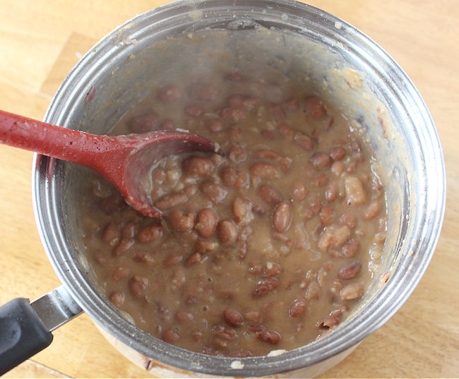 Pot of refried beans being stirred with a red spoon.