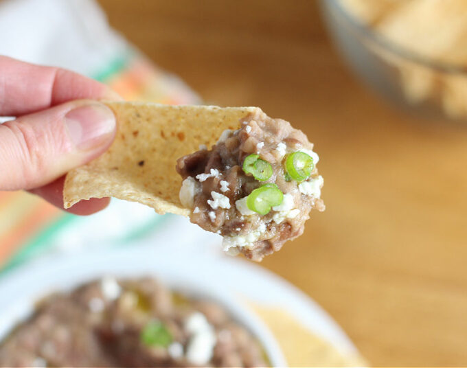 Hand holding a tortilla chip with bean dip and scallions on it.