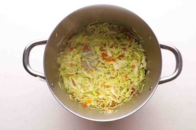 Sauteing vegetables and cabbage in a pot.