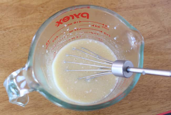 Measuring cup with milk and egg being whisked.
