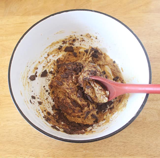 Cookie dough in a large white bowl being stirred with a red spoon.