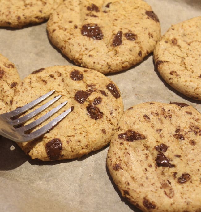 Fork pressing on a baked chocolate chip cookie.