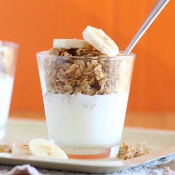 Small glass with yogurt on the bottom and granola on top.