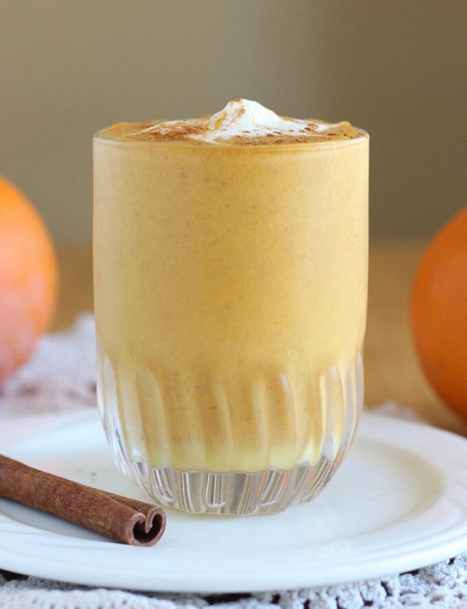 Side shot of pumpkin smoothie with a cinnamon stick laying beside it.