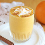 Pumpkin smoothie with whipped cream on top on a white plate.
