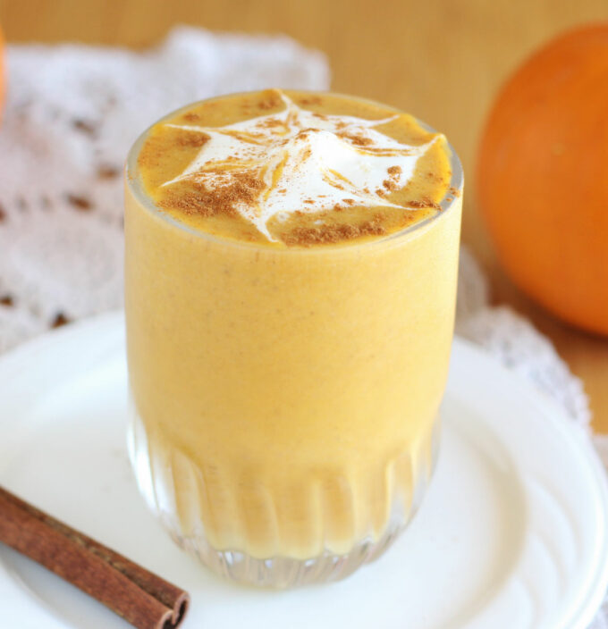 Pumpkin smoothie with whipped cream on top on a white plate.