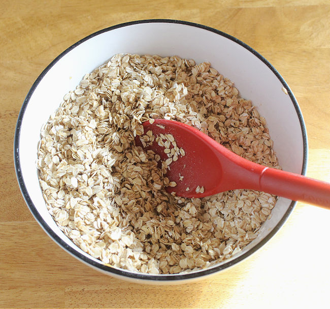 Large red spoon stirring oats in a bowl.
