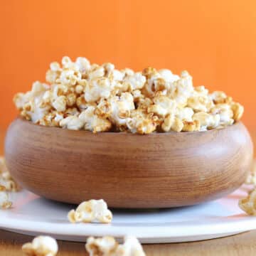 Brown bowl filled with caramel corn on a white plate.