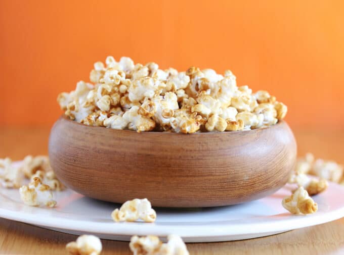 Brown bowl filled with caramel corn on a white plate.