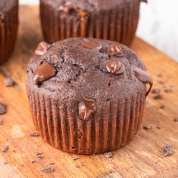 Chocolate cupcake with melted chocolate chips on a wood cutting board.