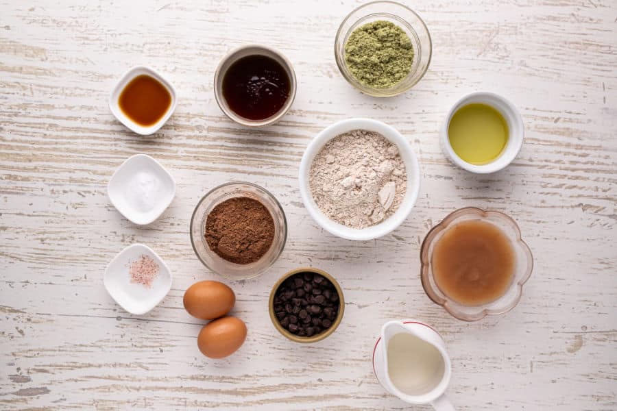 Various ingredients laid out on a table, including flour, cocoa, eggs, and applesauce.
