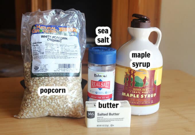 Various ingredients on a table, including popcorn, salt, maple syrup, and butter.