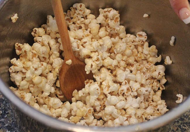 Popcorn being stirred with a wood spoon in a large pot.