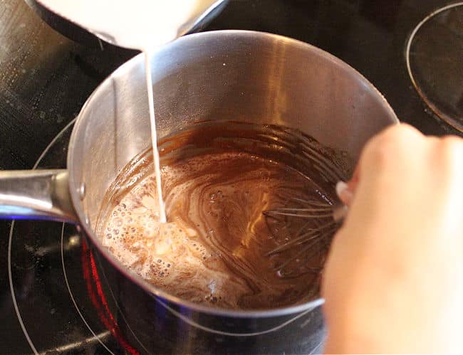 Milk being slowly poured into a pot with chocolate in it.