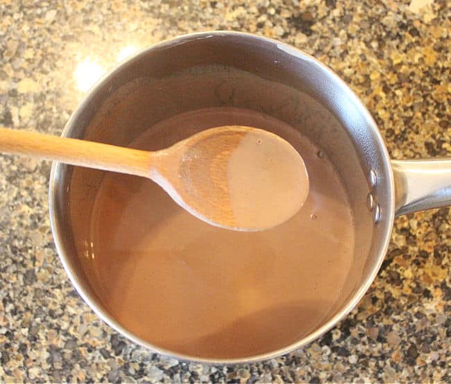 Hot chocolate in a pot being stirred with a wooden spoon.