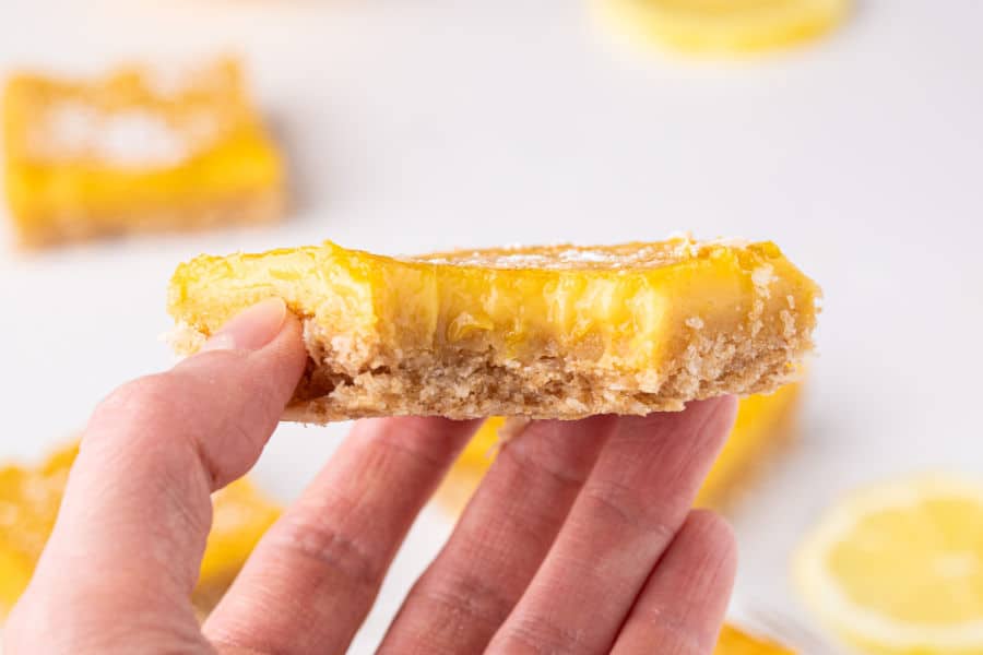 Hand holding a lemon bar with a bite taken out.