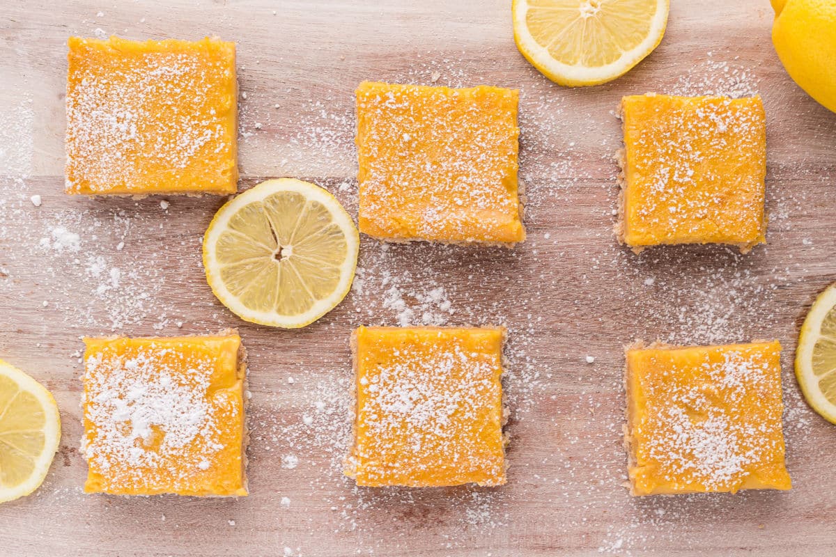 Lemon bars laid out on a board surrounded by lemon slices.