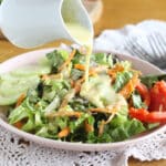 Plate full of lettuce and raw vegetables with a dressing being poured over the top.