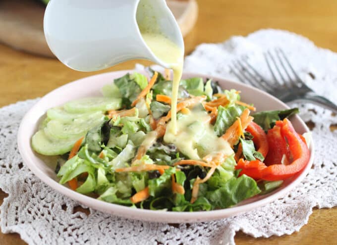 Salad and vegetables on a plate with dressing being poured over the top.