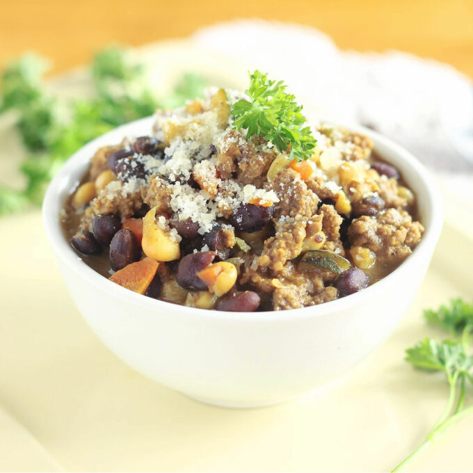 Chili in a white bowl topped with parmesan and parsley.