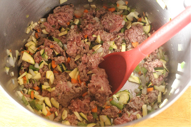 Ground beef and vegetables in a large steel pot.