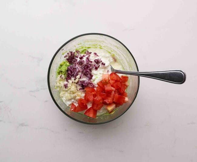 Mixing cottage cheese, tomato, red onion, and garlic in a bowl.