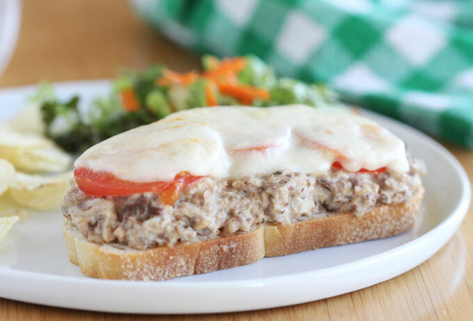 Sandwich topped with sardines, tomato, and cheese.