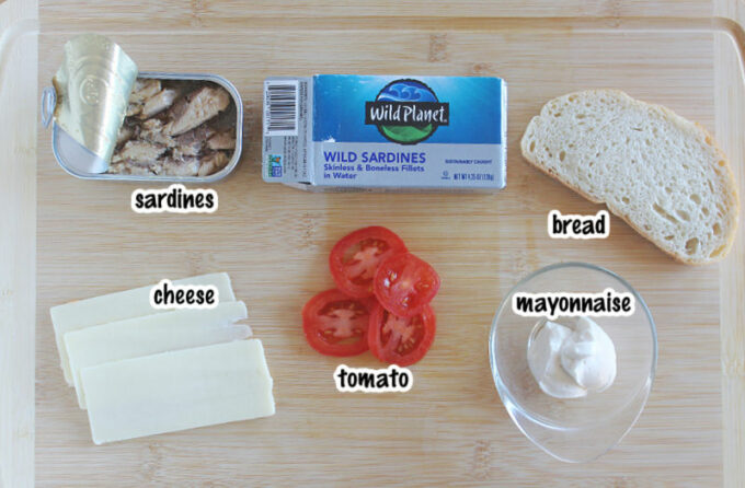 Various ingredients laying on a cutting board, including sardines and mayo.
