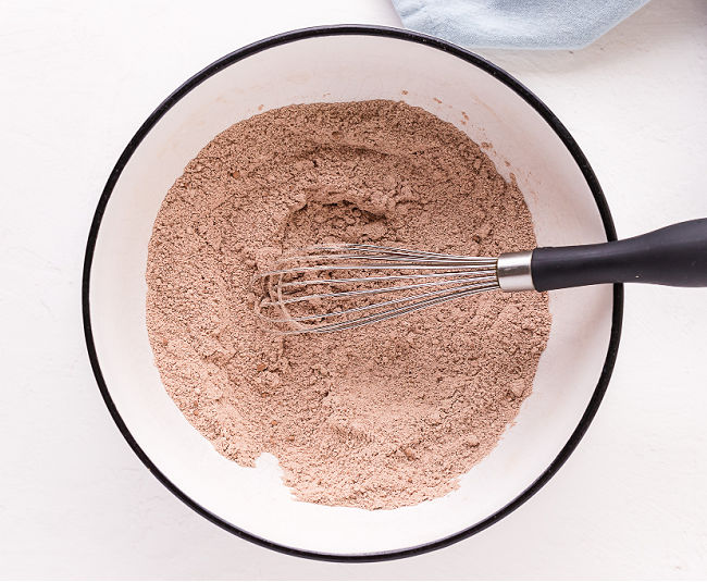 Flour, cocoa powder, and baking soda being whisked in a white bowl.