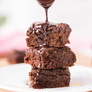 Stack of three brownies being drizzled with chocolate sauce.