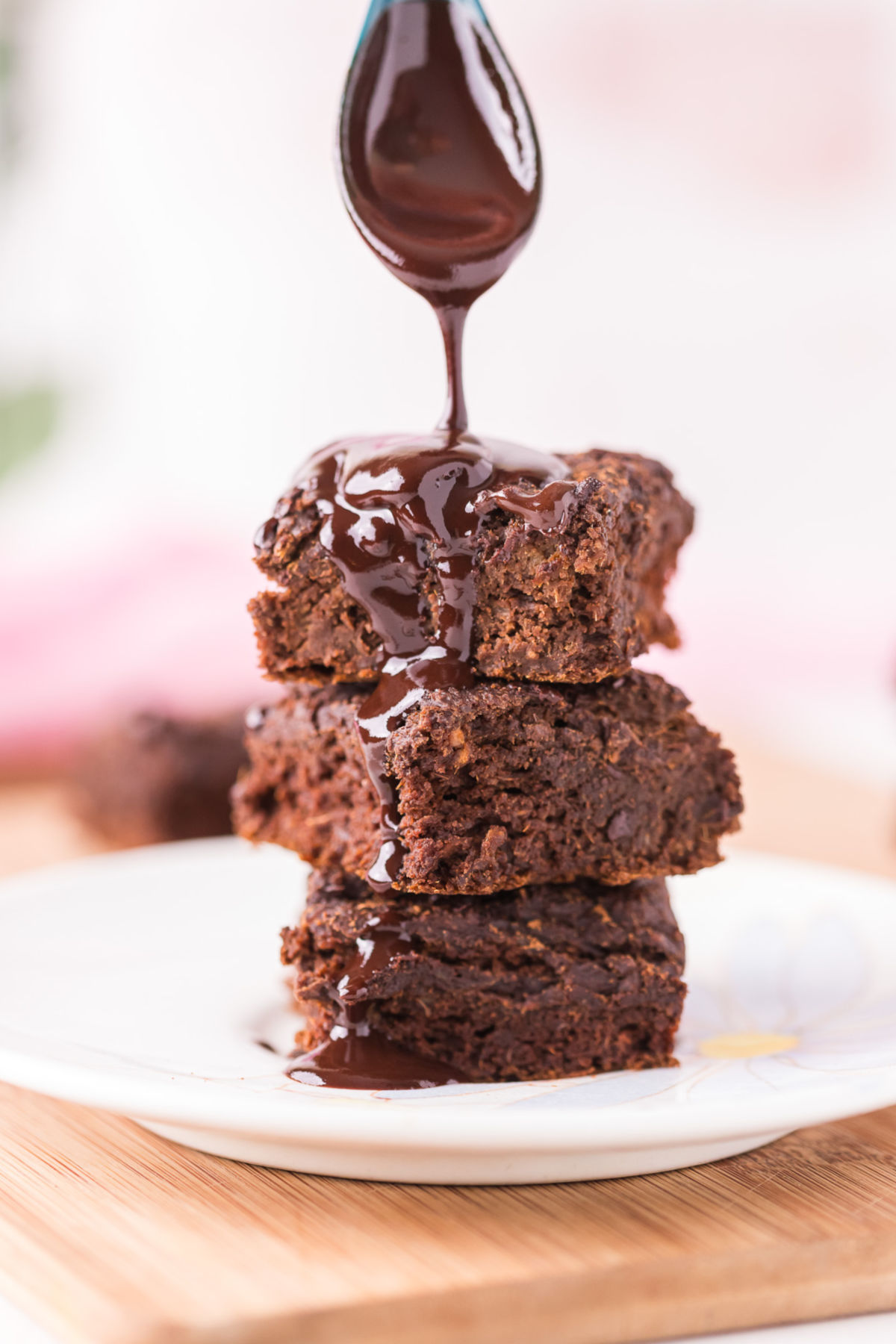 Stack of three brownies being drizzled with chocolate sauce.