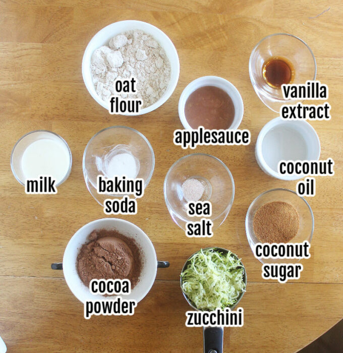 Various ingredients laid out on a wood table, including oat flour and cocoa powder.