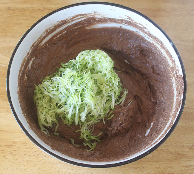 Chocolate brownie batter and grated zucchini in a white bowl.