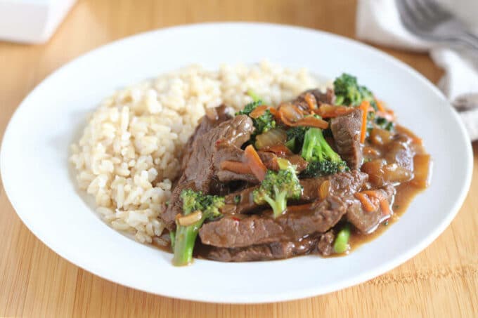 Plate of meat, broccoli, carrots, and rice on a white plate with a wooden counter.