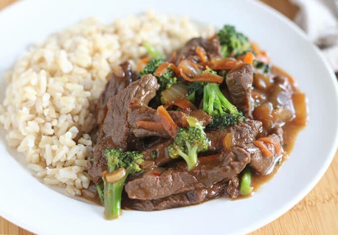 Close-up of meat with vegetables and brown rice on a white plate.