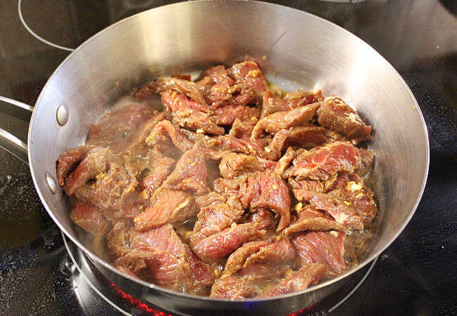 Sliced meat cooking in a stainless steel pan.
