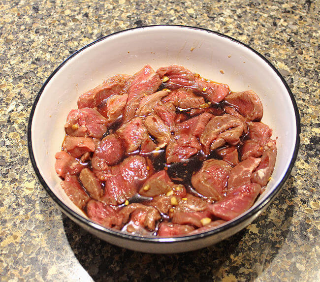 Sliced meat marinating in a large white bowl.