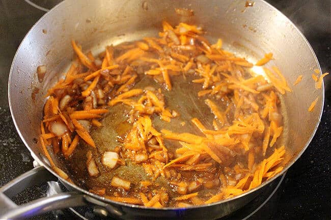 Onions and carrots cooking in a large pan.