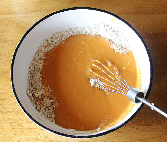 Flour, pumpkin, and milk being mixed together in a bowl on a wood table.
