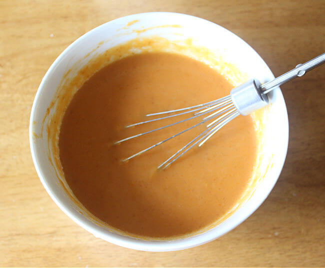 Pumpkin and milk being whisked in a large white bowl.