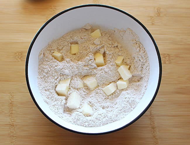 Flour and chunks of butter in a bowl on a wood counter.